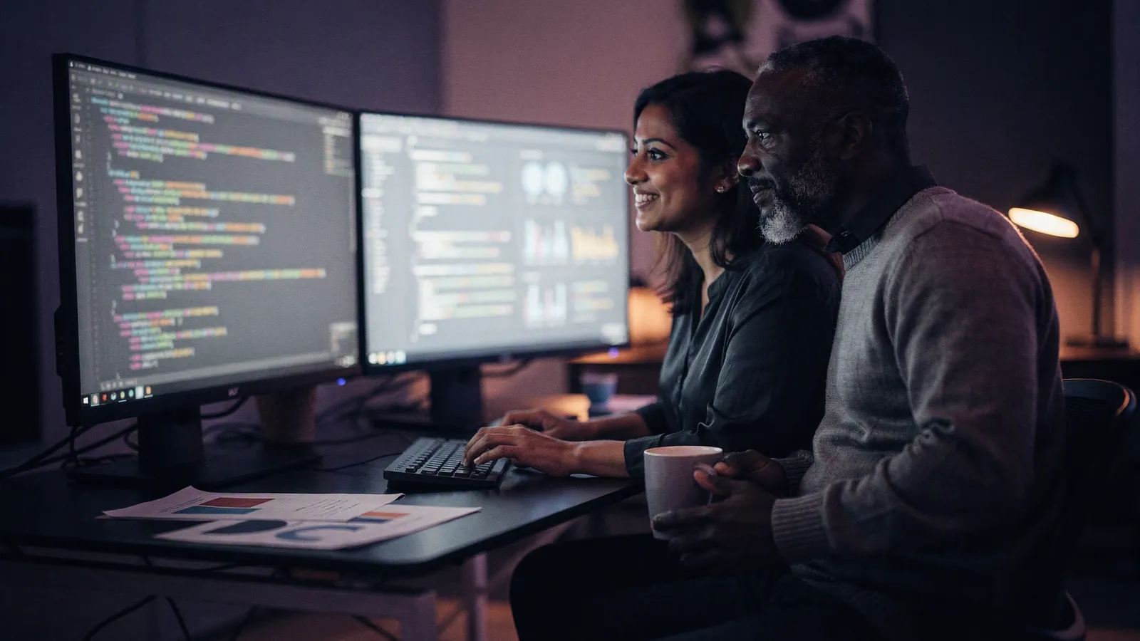 Two people reviewing code and dashboards together, side by side at a desk